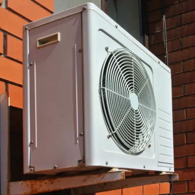 An outdoor condenser unit mounted on a bracket against a brick wall