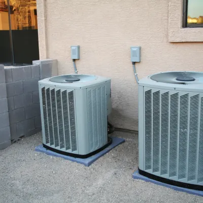 Two outdoor condenser units installed next to a stucco home